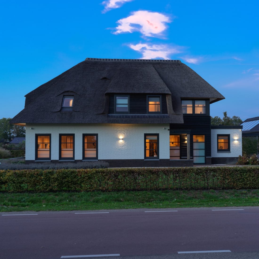 vrijstaande woning met rieten kap en buitenverlichting overdag.